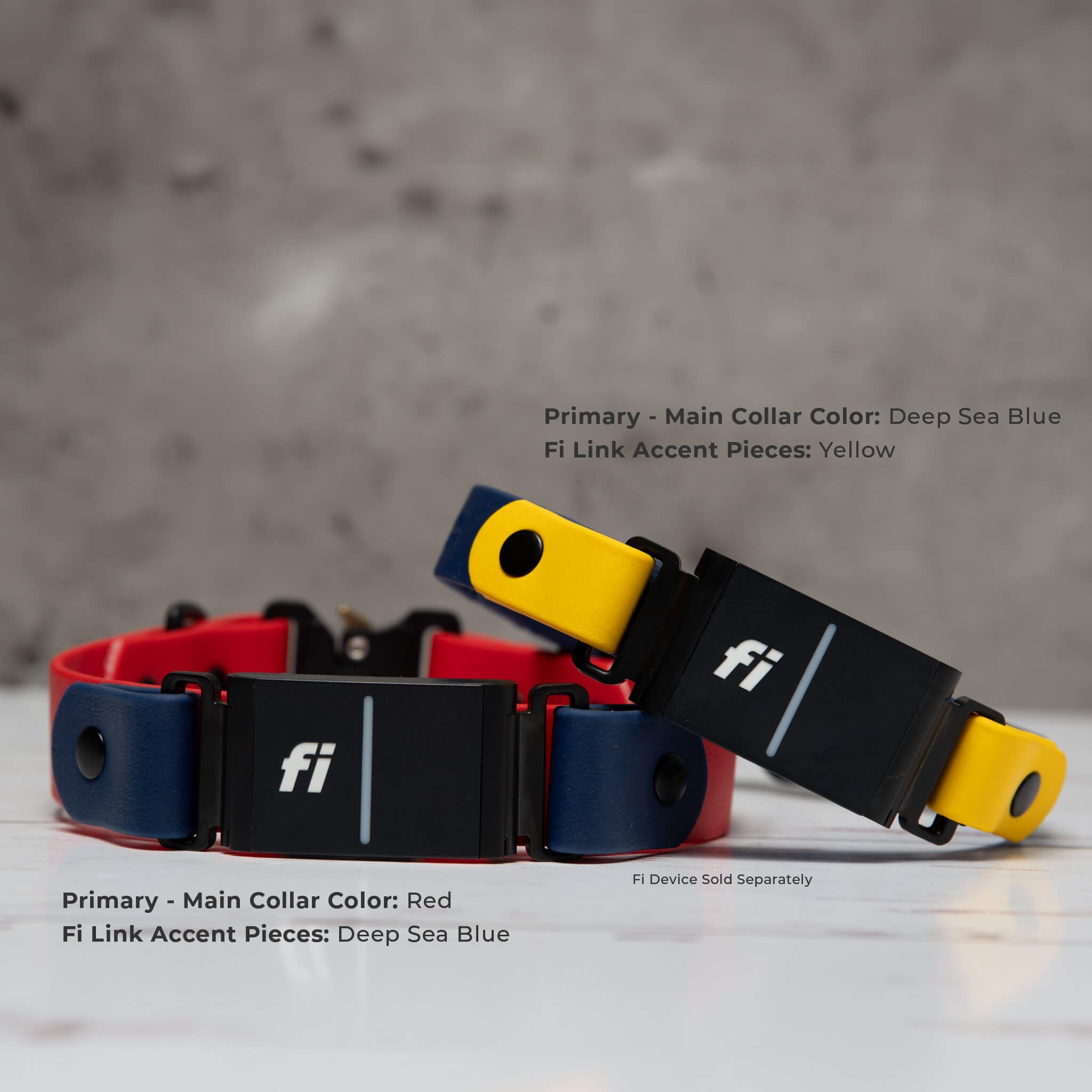 Two Biothane Fi dog collars shown on a light marble surface against a textured gray wall. One collar is red and deep sea blue with black Fi links; the other is deep sea blue and yellow with black fi links.