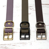 Three collars with gold, black, and silver hardware on a white wooden surface
