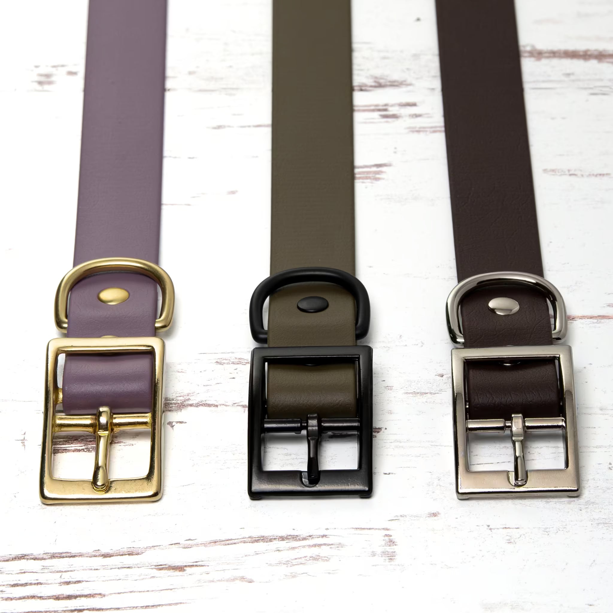 Three collars with gold, black, and silver hardware on a white wooden surface