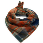A plaid pet bandana scarf in orange, blue, green, and beige, styled with a small metal snap and a brown leather brand tag on a white background.