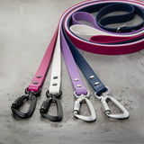 Four BioThane® dog leashes with aluminum carabiner hardware in matte black and silver shown on a grey cement background.