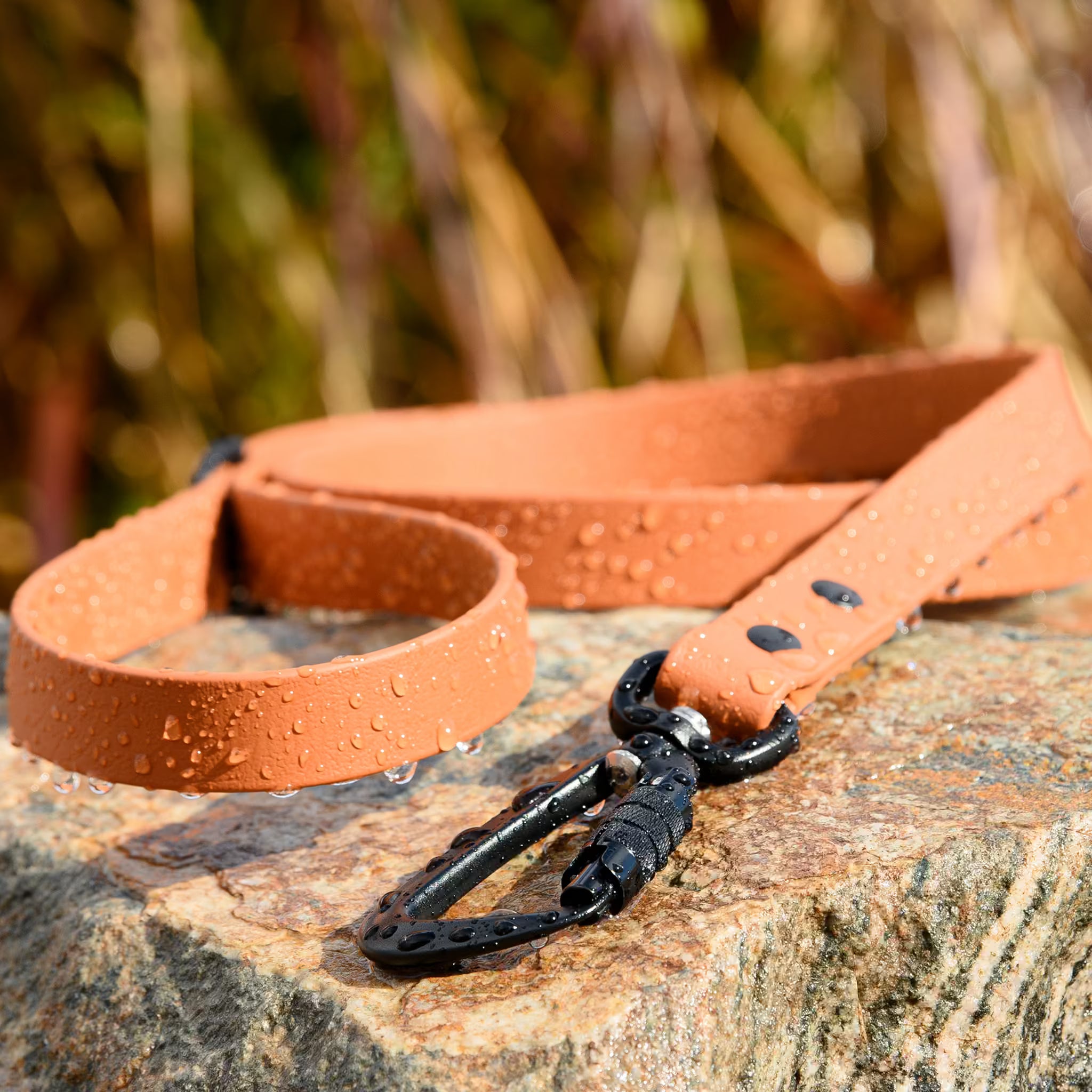 Waterproof dog leash in caramel color with water droplets and black carabiner on stone surface